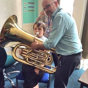 Deaf young person being assisted to play the tuba by a brass teacher